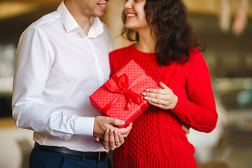 Man gives to his woman a gift box with red ribbon. A loving couple cuddles and celebrating Valentine's Day in the restaurant. Valentine's Day, holiday and surprise concept. Relationship and love.