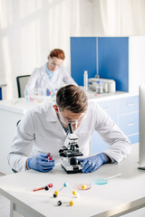 selective focus of genetic consultant holding test tubes and using microscope in lab