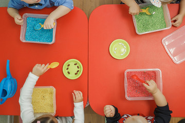 Children play educational games with a sensory bin in kindergarten. - obrazy, fototapety, plakaty