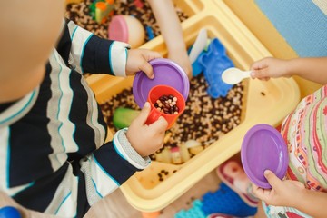 Children play educational games with a sensory bin in kindergarten - obrazy, fototapety, plakaty