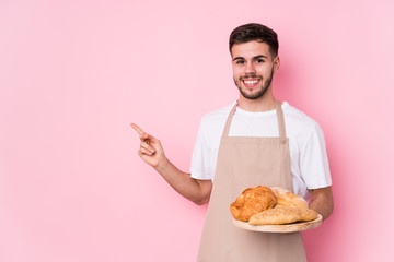 Young caucasian baker man isolated smiling and pointing aside, showing something at blank space.