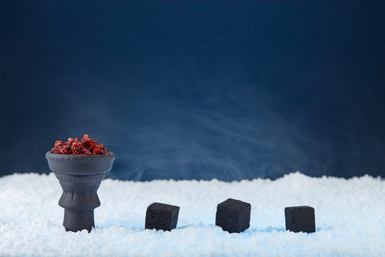 Shisha apple-scentedin a black bowl prepared for Smoking a hookah and three cubes of coconut coals standing on white crystals on a dark blue abstract background. Copy space.