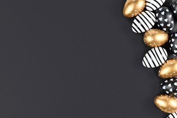 Flat lay with golden, black and white easter eggs painted with stripes, hearts and dots on black...