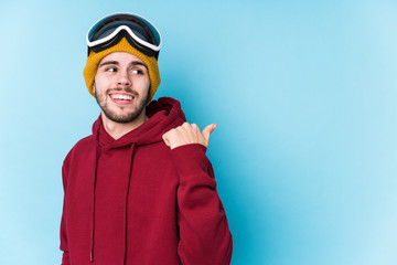 Young caucasian man wearing a ski clothes isolated points with thumb finger away, laughing and carefree.