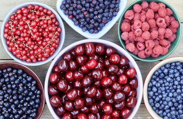 Bowls with fresh garden and forest berries: raspberry, sweet cherries, red and black currant, blueberry, purple shadberry overhead on the wooden table, flat lay, from above top view, empty space