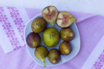 lots of ripe figs in a white plate on a white wooden background with a pink towel. the concept of healthy eating. vegan. live vitamins. cut figs. the view from the top. space for text