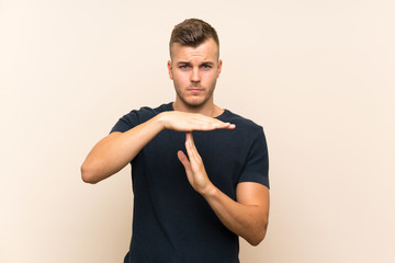 Young handsome blonde man over isolated background making time out gesture