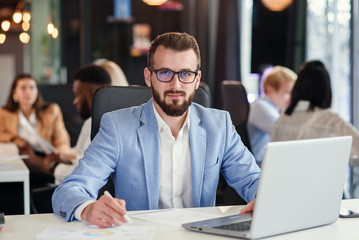 Close up handsome confident bearded office manager in business suit works with laptop at the office room.