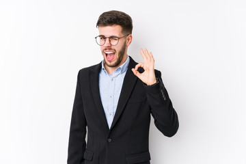 Young caucasian business man posing in a white background isolated Young caucasian business man winks an eye and holds an okay gesture with hand.
