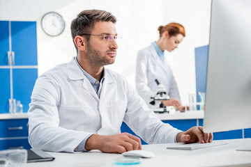 selective focus of molecular nutritionist using computer and his colleague using microscope on...