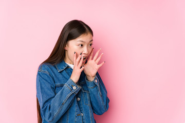 Young chinese woman posing in a pink background isolated shouts loud, keeps eyes opened and hands tense.