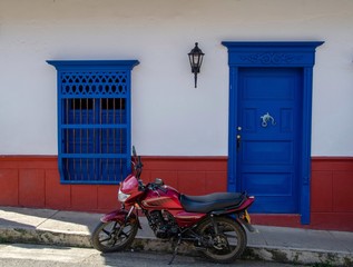 Puerta y ventana en madera azul con zocalo rojo sobre fachada blanca