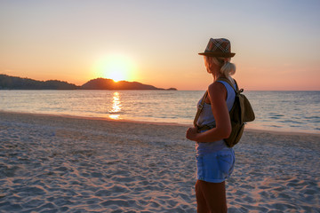 Young woman standing on the beach in sea and looking to sunset. She is enjoying serene ocean nature...