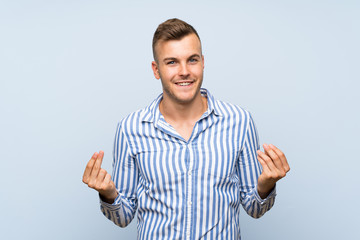Fototapeta premium Young handsome blonde man over isolated blue background making money gesture