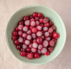 Frozen cranberry in green bowl close up. White linen cloth background view. Healthy eating concept