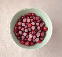 Frozen cranberry in green bowl close up. White linen cloth background view. Healthy eating concept