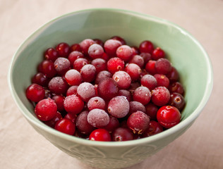 Frozen cranberry in green bowl close up. White linen cloth background view. Healthy eating concept