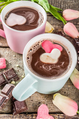 Valentines day treat ideas, two cups hot chocolate drink with marshmallow hearts red pink white color with chocolate pieces, sugar sprinkles, old wooden background copy space top view