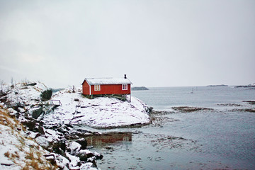 Traditional red rorbu house of Lofoten islands built on a rock, winter landscape and sea around.