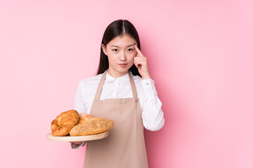Young chinese baker woman isolated pointing temple with finger, thinking, focused on a task.
