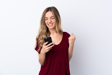 Naklejka premium Young woman over isolated white background with phone in victory position