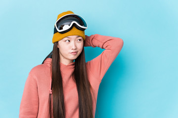 Young chinese woman wearing ski clothes isolated touching back of head, thinking and making a choice.