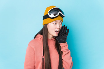 Young chinese woman wearing ski clothes isolated shouting and holding palm near opened mouth.