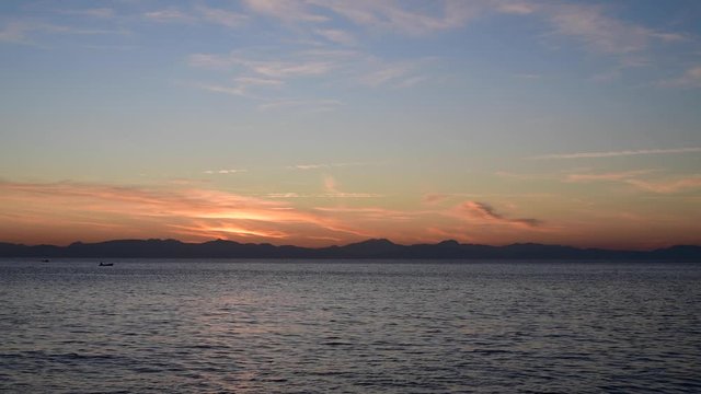 View from Elba Island over Corsica at sunset. Calm sea waters surface. Serene orange pastel tone. Small boat fishing.