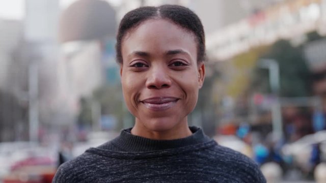 Slow motion of one young African woman looking at camera smile in the city urban background beautiful black young lady portrait face the camera with tears in eyes outdoor real people 4k footage