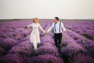 Happy newlyweds running along blooming lavender field at sunset
