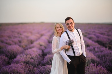 Happy newlyweds stand in blooming lavender field at sunrise