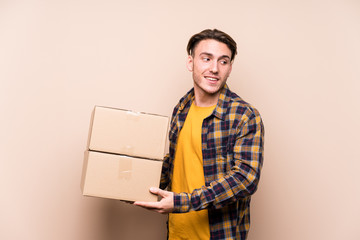 Young caucasian man holding boxes looks aside smiling, cheerful and pleasant.