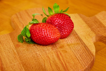 Two ripe juicy strawberries with green leaves lie side by side on a cutting Board natural wood texture