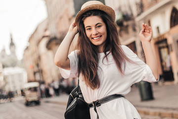 Young stylish woman walking on the old town street, travel with backpack, straw hat, wearing trendy...