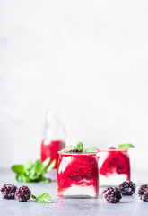 Glass jars of healthy layered berries and yogurt smoothie. Mix berry smoothie with raspberry, blackberry and yogurt. Wellbeing and weight loss concept. Selective focus, toned image.