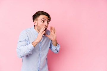 Young caucasian man posing in a pink background isolated shouts loud, keeps eyes opened and hands...
