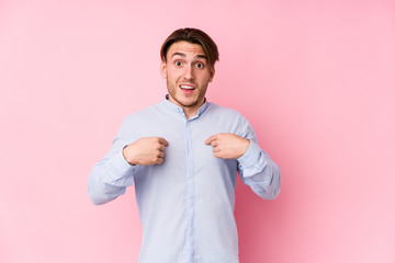 Young caucasian man posing in a pink background isolated surprised pointing with finger, smiling broadly.