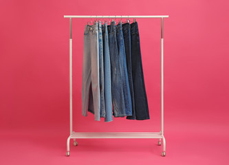 Rack with stylish jeans on pink background