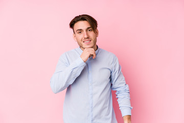 Young caucasian man posing in a pink background isolated smiling happy and confident, touching chin with hand.