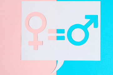 male and female symbols and an equal sign in white dialogue box cut out of paper on a pink and blue...