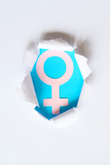 pink female symbol on the blue background sticking out of a hole in the white paper