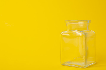 Open empty glass jar on yellow background, space for text