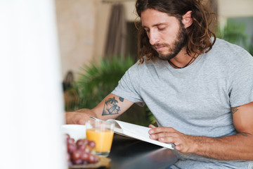 Man sit at the table indoors at home have a breakfast reading book.