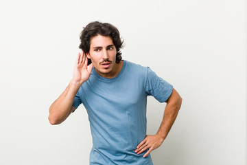 Fototapeta premium Young handsome man against a white background trying to listening a gossip.