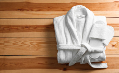 Clean folded bathrobe and slippers on wooden background, top view. Space for text