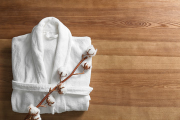 Clean folded bathrobe and branch of cotton on wooden background, top view. Space for text