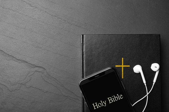Bible, phone and earphones on black background, top view with space for text. Religious audiobook