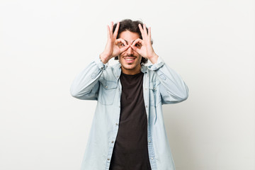 Young handsome man against a white background showing okay sign over eyes