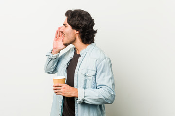 Young cool man drinking a coffee shouting and holding palm near opened mouth.