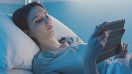 Young patient lying in bed and connecting with a tablet at night